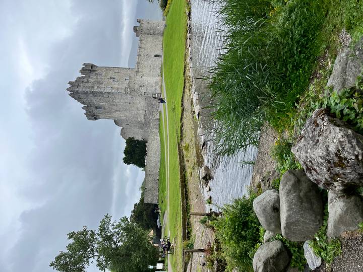 Old stone castle by a river with grassy surroundings.