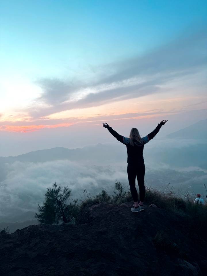 Personne debout avec les bras levés contemplant un paysage pittoresque et brumeux au lever ou au coucher du soleil.