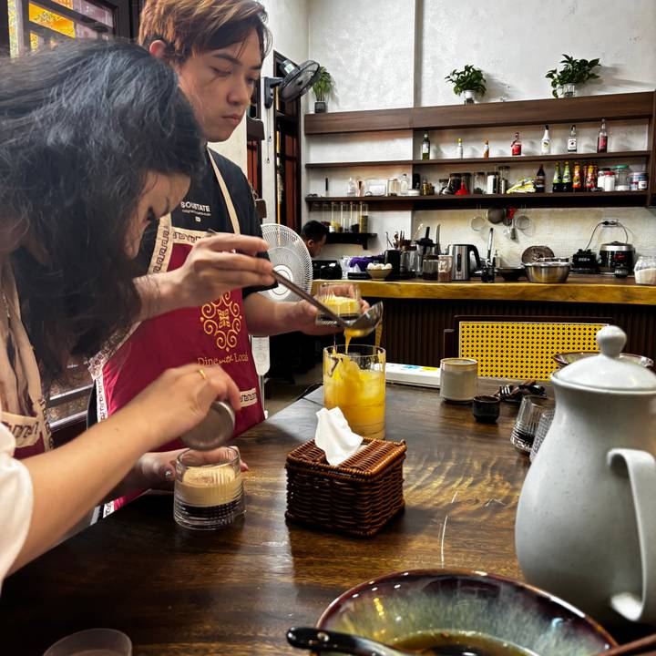 Une personne préparant une boisson au café traditionnelle dans un café animé.