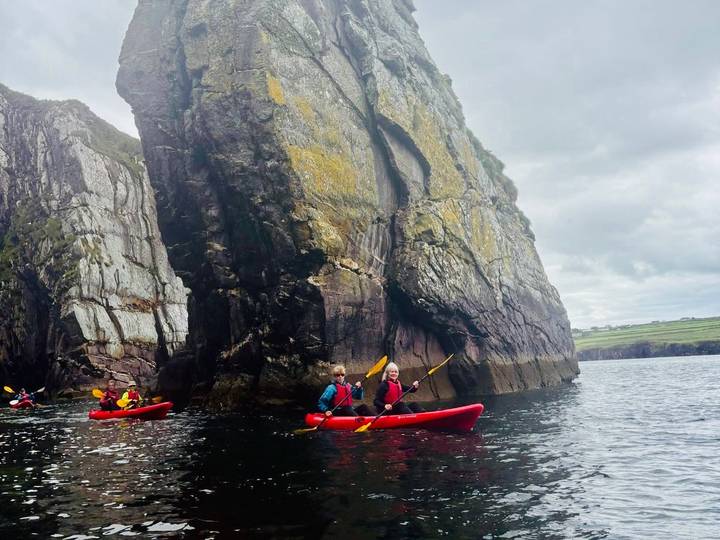 People kayaking near a large rocky outcrop in the sea.