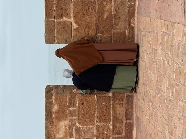 Two people standing at a stone wall, gazing at the sea.