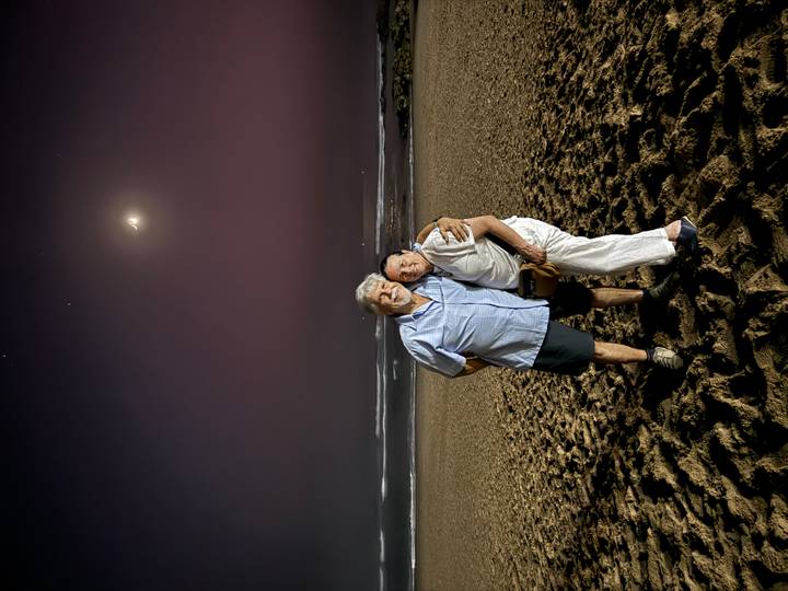 Couple posing on a beach at night with a crescent moon.