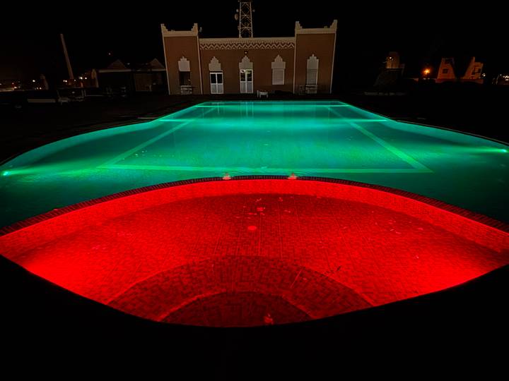 Swimming pool illuminated with red and green lights at night.
