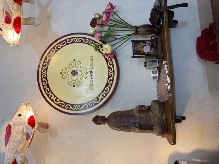 Dekorative Wand mit einer 'Dine with Locals' Plakette und einer Buddha-Statue.