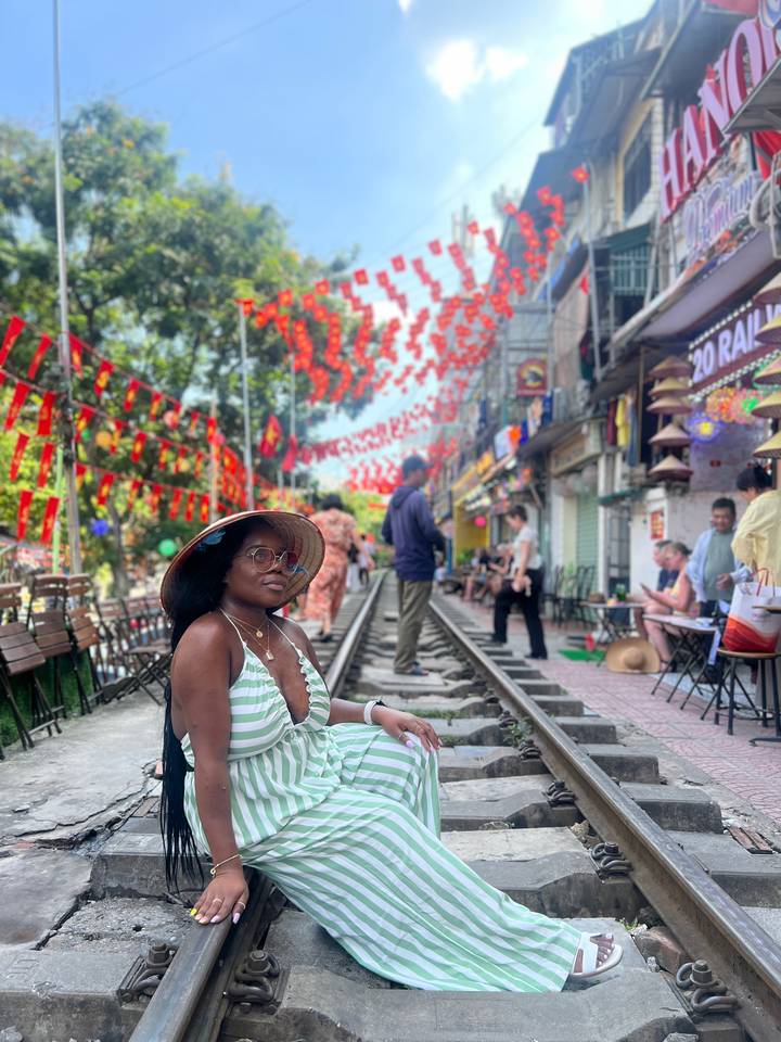 Femme posant devant des drapeaux colorés et une voie ferrée.