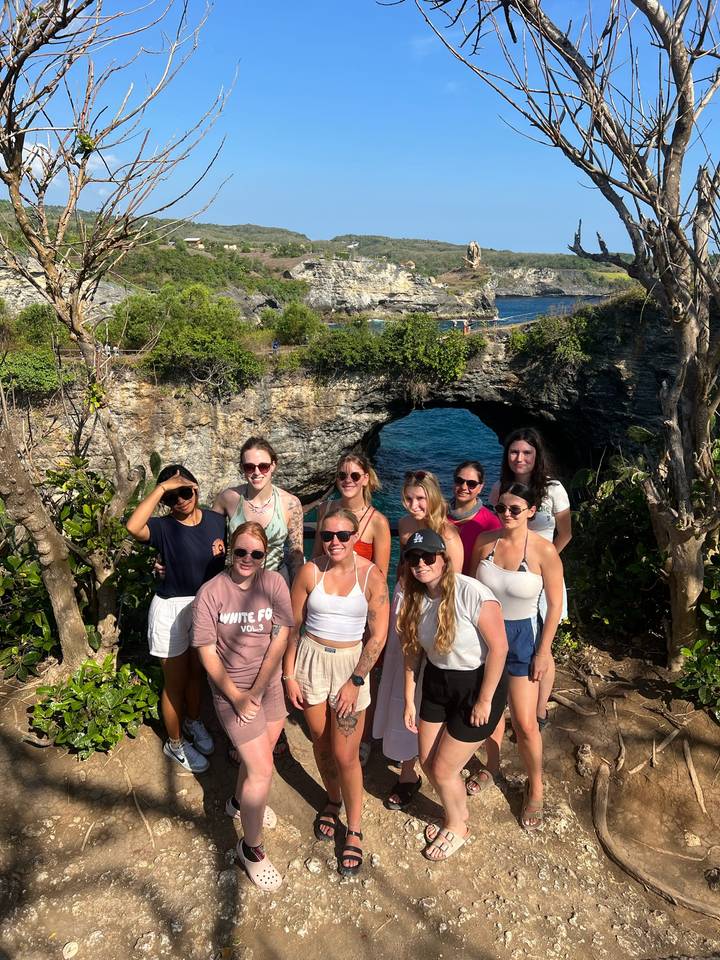 Un groupe de personnes posant devant une arche rocheuse naturelle au-dessus de l'océan.