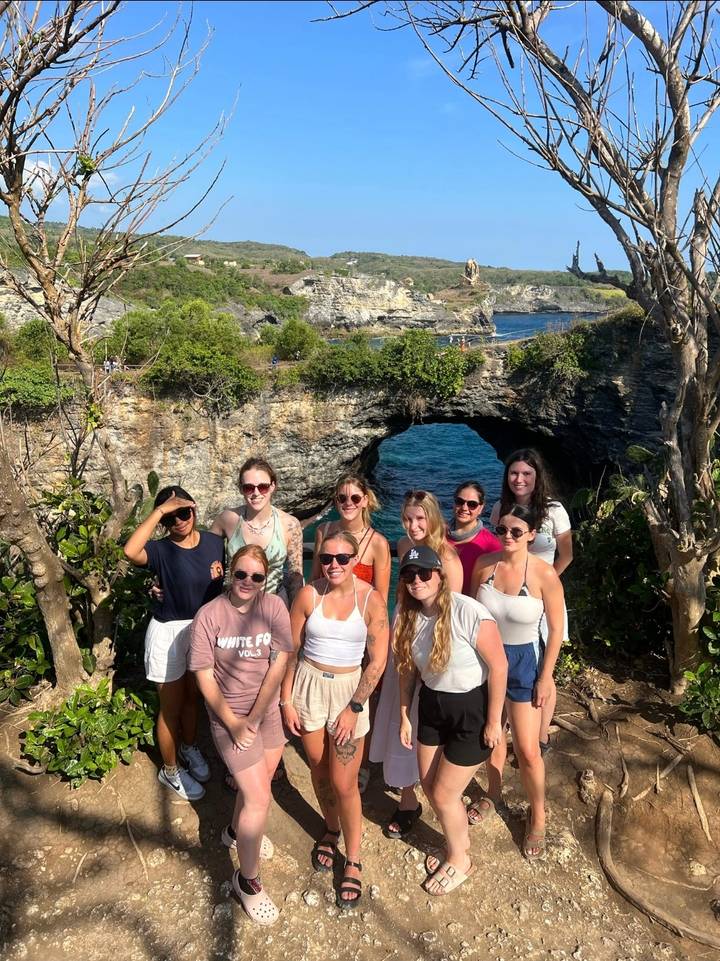 Groupe de touristes posant avec un pont naturel en arrière-plan.
