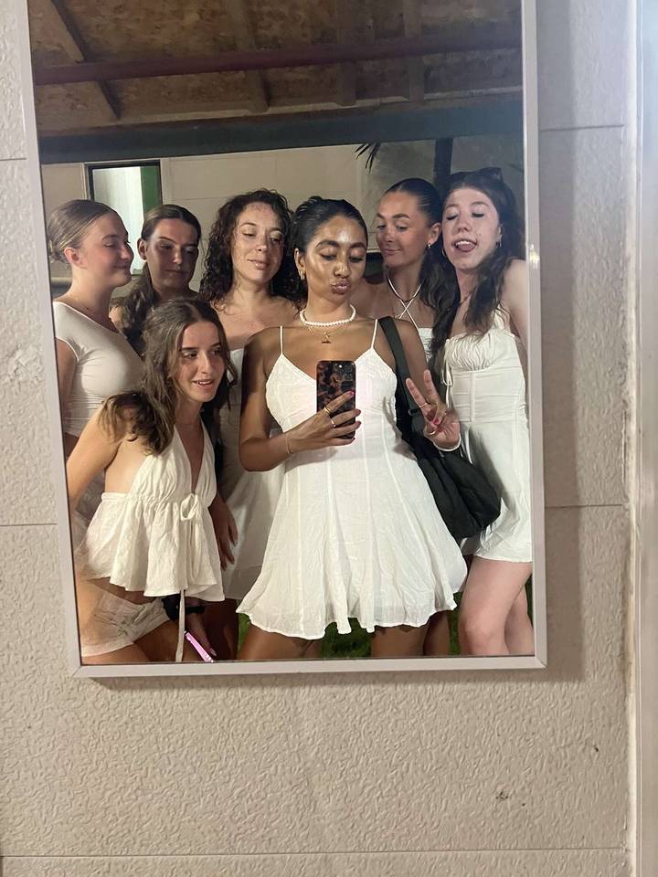 Group of people taking a selfie in a mirror, wearing white outfits.