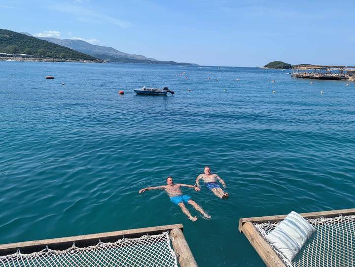 Deux personnes nageant dans une mer bleue claire avec des bateaux à proximité.