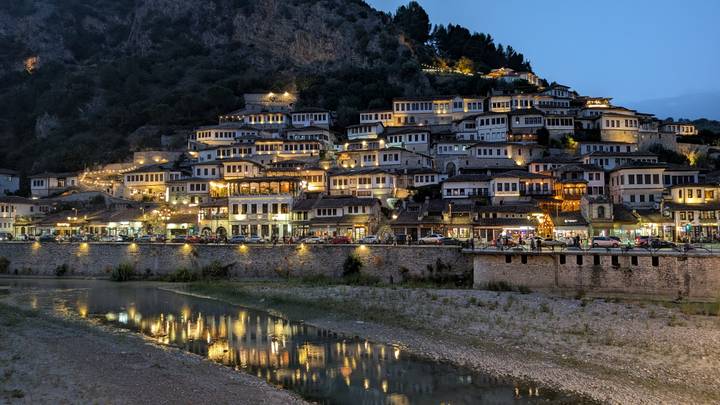 Vue nocturne de Berat, mettant en valeur les maisons historiques illuminées le long de la rivière.