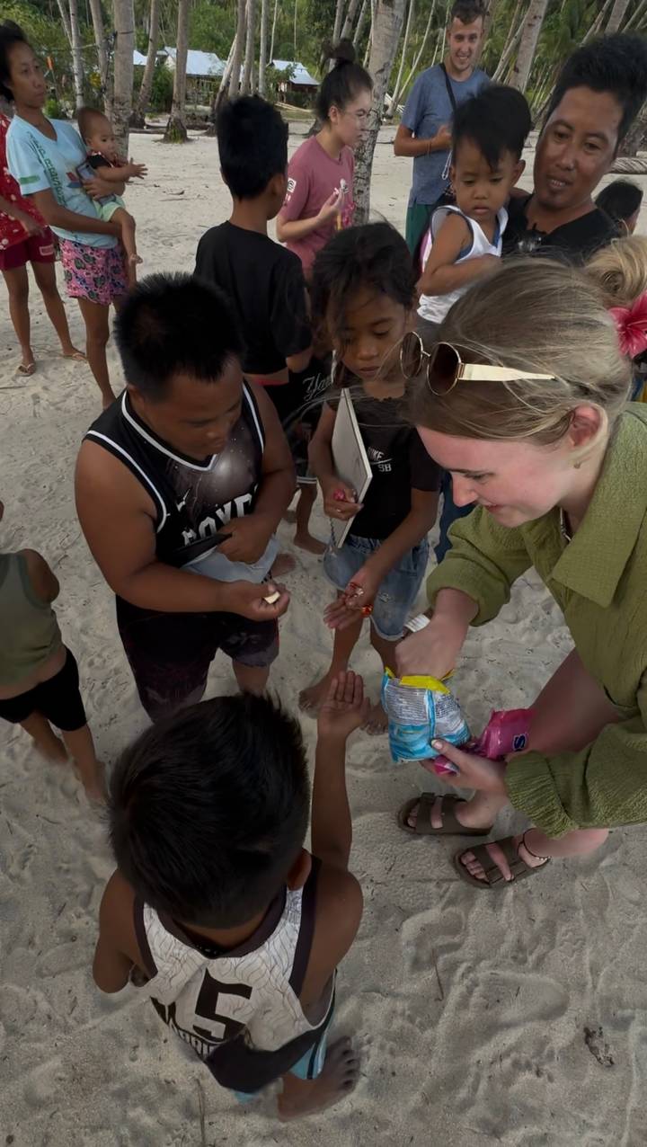Person interacting with local children on a sandy beach.