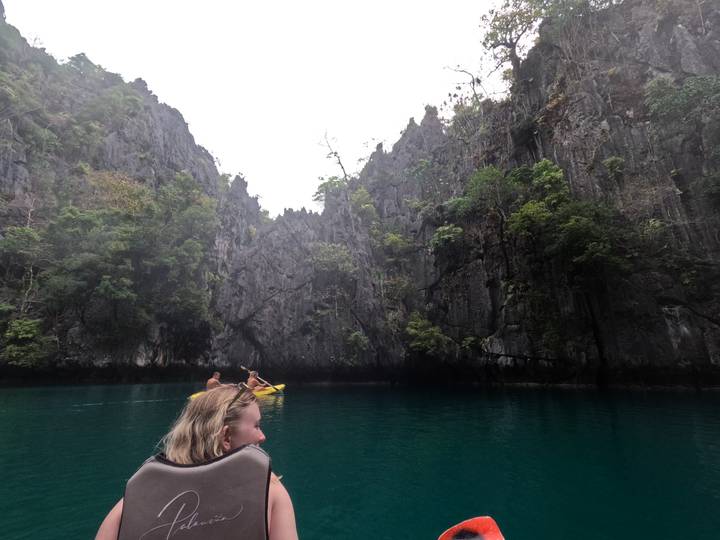 People kayaking through a rocky waterway with cliffs and lush vegetation.