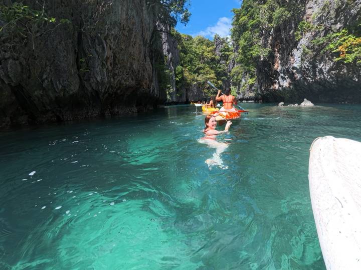 People kayaking and swimming in a turquoise blue waterway.