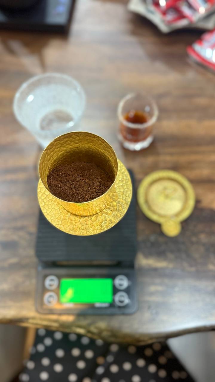 Close-up of coffee grounds in a golden container on a wooden table.
