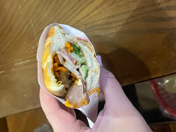 A hand holding a half-eaten sandwich wrapped in paper.