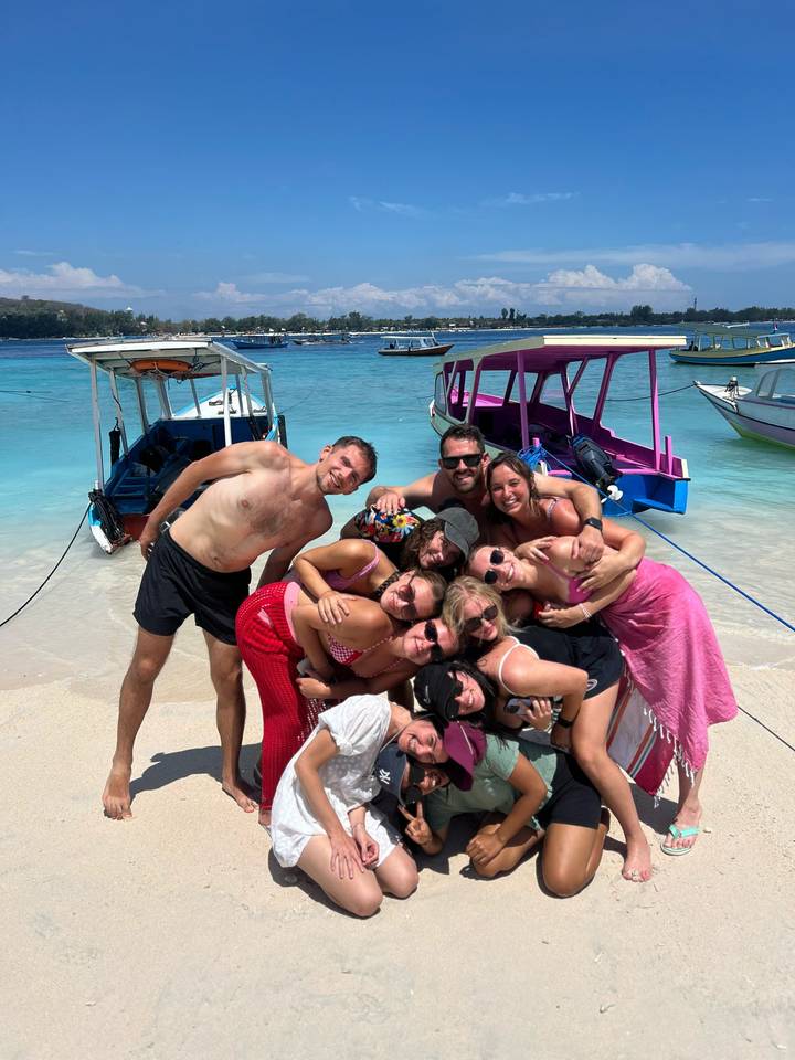 Groupe de personnes posant joyeusement sur une plage avec des bateaux en arrière-plan.