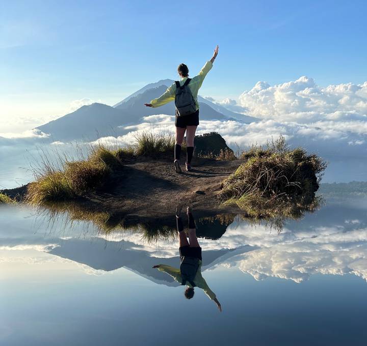 Personne debout sur un sommet de montagne avec un paysage nuageux et un reflet.