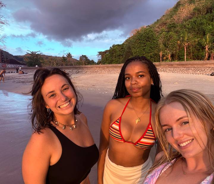 Trois femmes souriantes sur une plage au coucher du soleil.