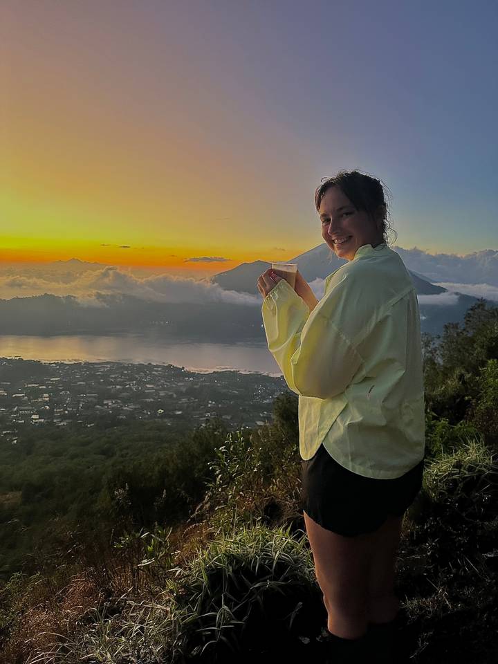 Femme tenant une boisson avec vue sur un coucher de soleil sur les montagnes.