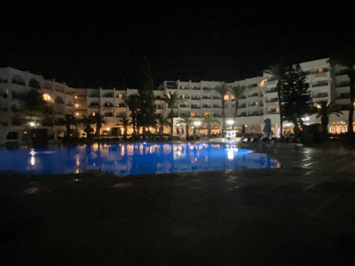 Vue nocturne d'un hôtel avec une piscine reflétant les lumières.