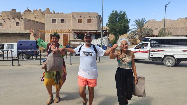 Trois personnes portant des sacs de courses, souriantes à l'extérieur.