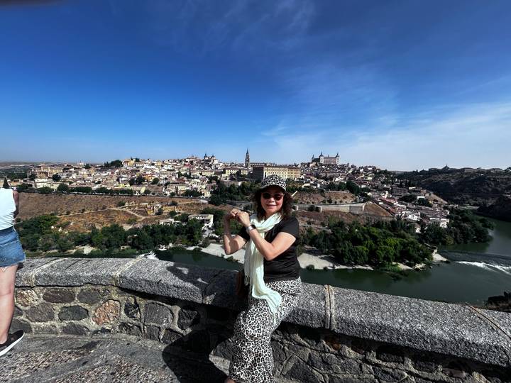 Femme posant près d'un mur de pierre avec vue sur une ville de l'autre côté d'une rivière.