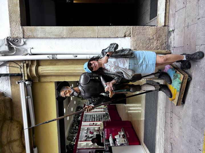 Femme posant avec une statue de Don Quichotte devant une boutique.
