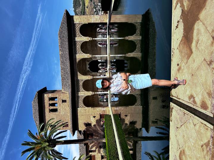 Femme debout près d'une piscine avec des arches réfléchissantes et une tour en arrière-plan.