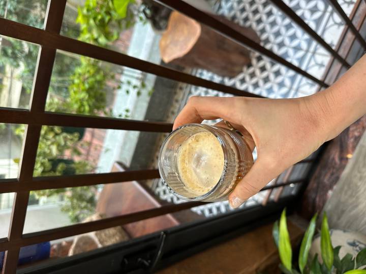 Person holding an espresso cup next to a window with a view of a courtyard.