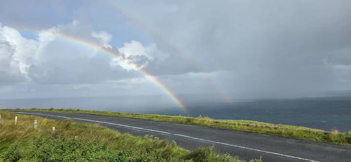 Arc-en-ciel double au-dessus d'une route de falaise et de l'océan.