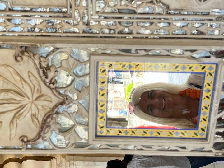 Eine Frau, die sich in einem Spiegel mit traditioneller indischer Dekoration spiegelt.