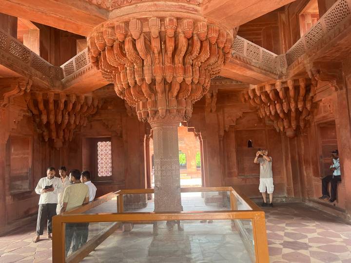 Innenraum von Fatehpur Sikri mit kunstvollen Säulen und Besuchern.