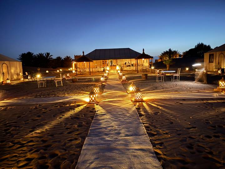 Camp du désert éclairé avec un sentier bordé de lanternes la nuit.