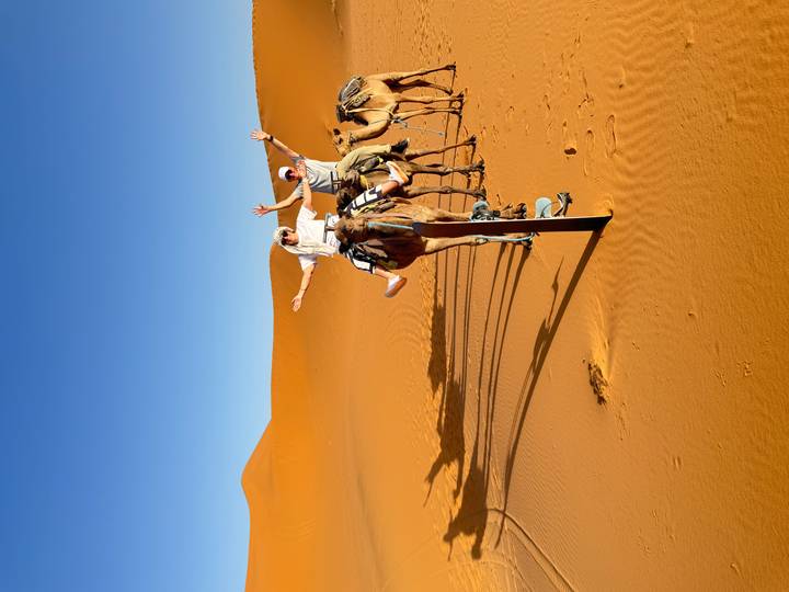 Deux personnes montant des chameaux dans le désert avec les bras levés.