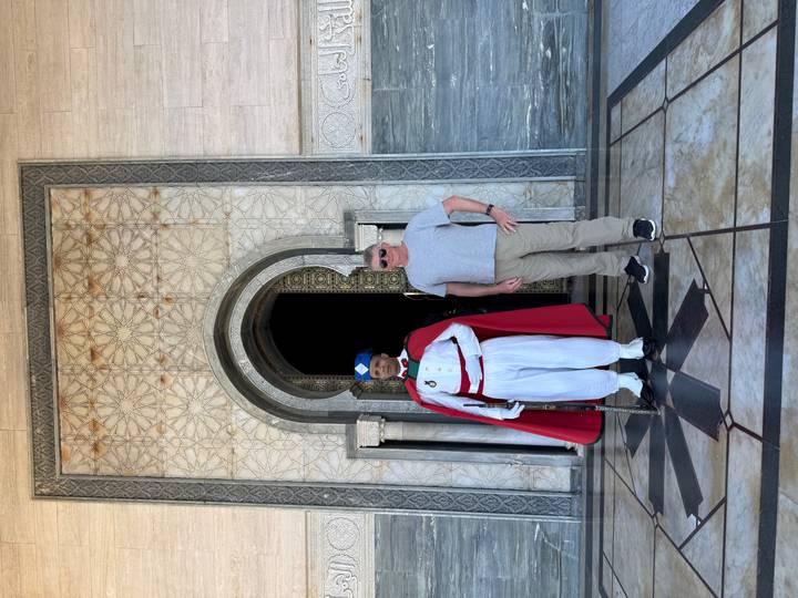 Touriste posant avec un garde traditionnel devant un bâtiment officiel.