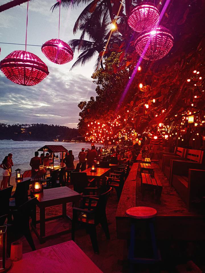 Zone de restauration en plein air éclairée par des lanternes rouges près de la mer.