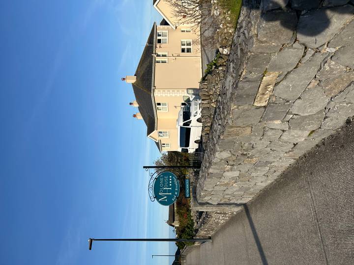 Maison avec un panneau et un bus garé dans une zone ensoleillée.