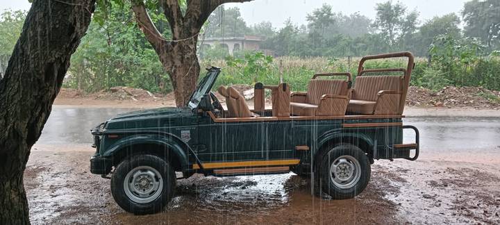 Jeep décapotable garé sous la pluie sur un chemin de terre.