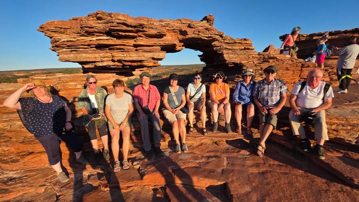 A group of tourists posing on rocky terrain with an arch formation in the background.