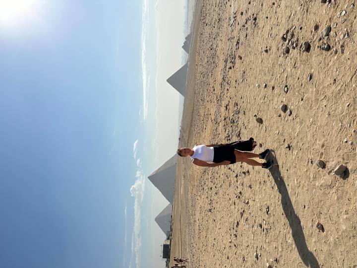 Une personne debout sur le plateau de Gizeh avec des pyramides au loin.