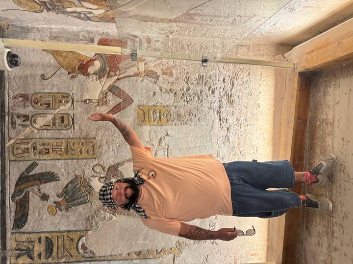 Personne posant près d'hiéroglyphes muraux égyptiens à l'intérieur d'une structure historique.