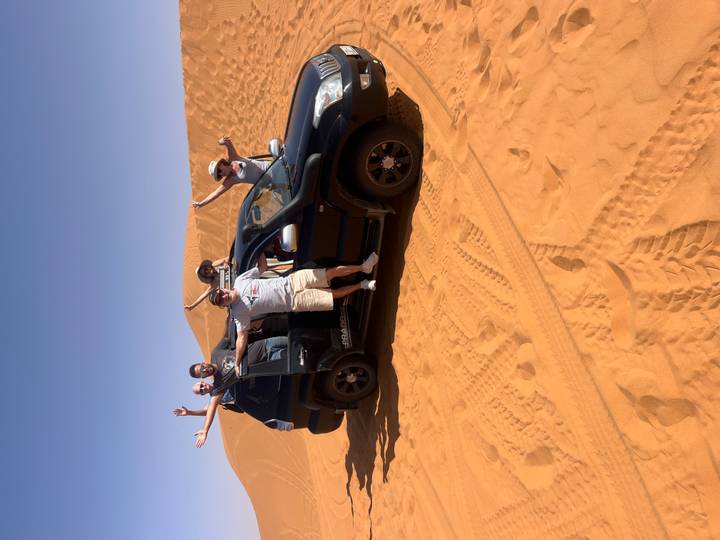 Group of people posing with an off-road vehicle in the desert.