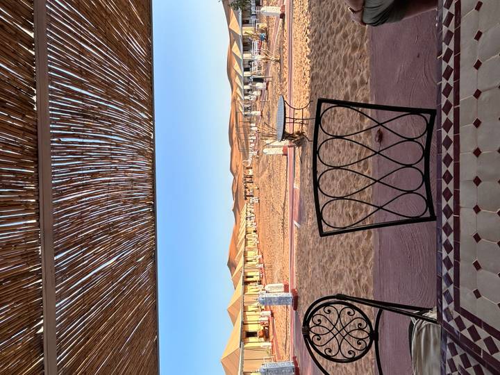 Campement dans le désert avec tentes et structure de toit tissée.
