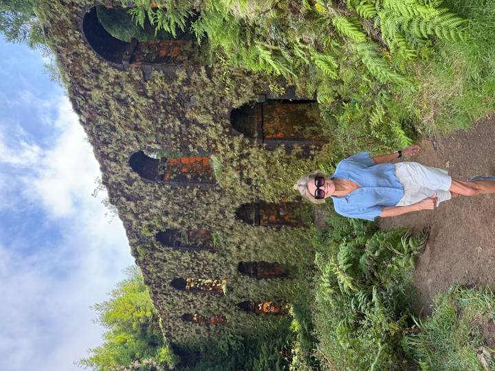 Une personne debout devant une ruine couverte de mousse avec des arches.
