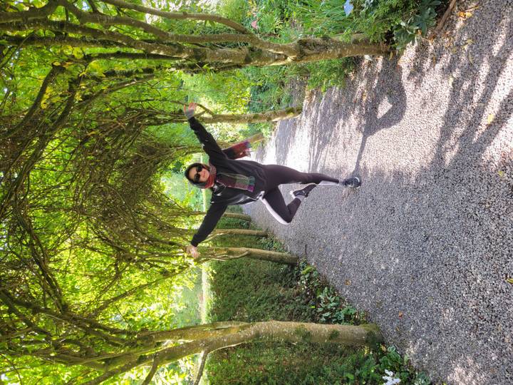 Une personne posant avec les bras étendus sous une canopée d'arbres.