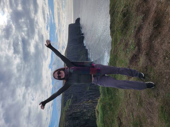 Une personne qui pose devant des falaises au bord de la mer.