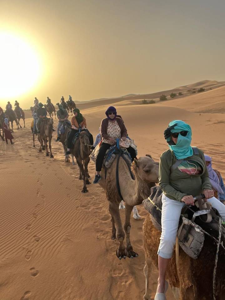Un groupe de personnes montant des chameaux dans un désert avec des dunes au coucher du soleil.