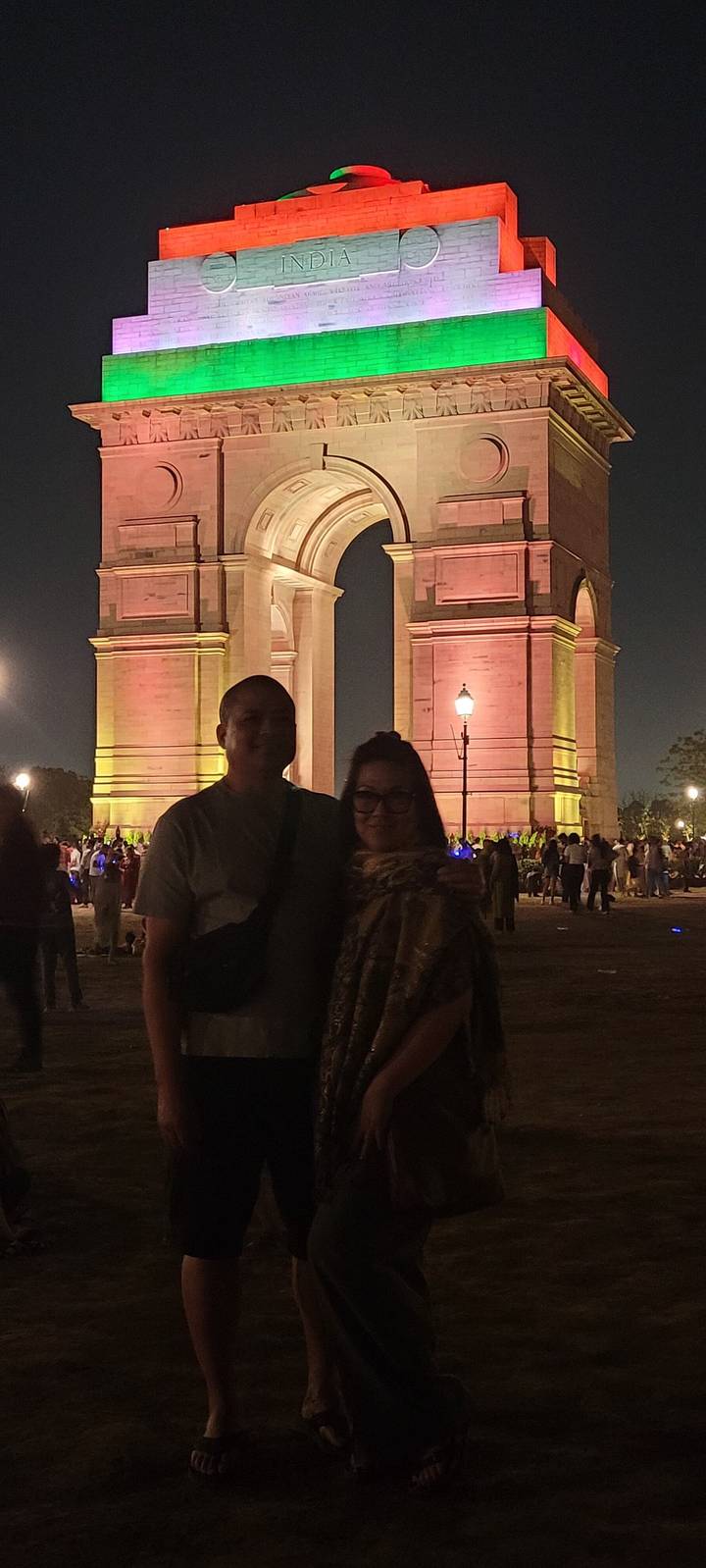 Couple debout devant la porte de l'Inde illuminée la nuit.