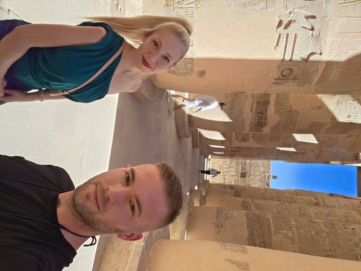 Deux touristes devant des piliers anciens avec des sculptures.