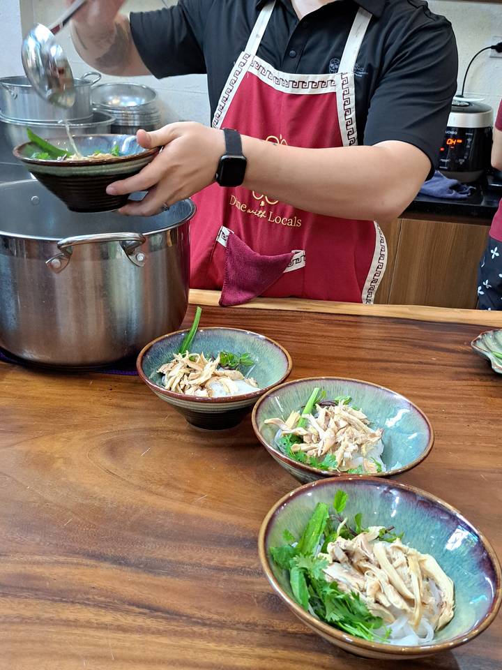 Personne servant une soupe de nouilles vietnamienne avec des herbes et des garnitures.
